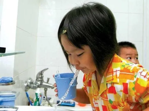 Một em bé đang súc miệng với sự hỗ trợ của người lớn, minh họa việc súc miệng nước muối pha loãng an toàn cho trẻ em.